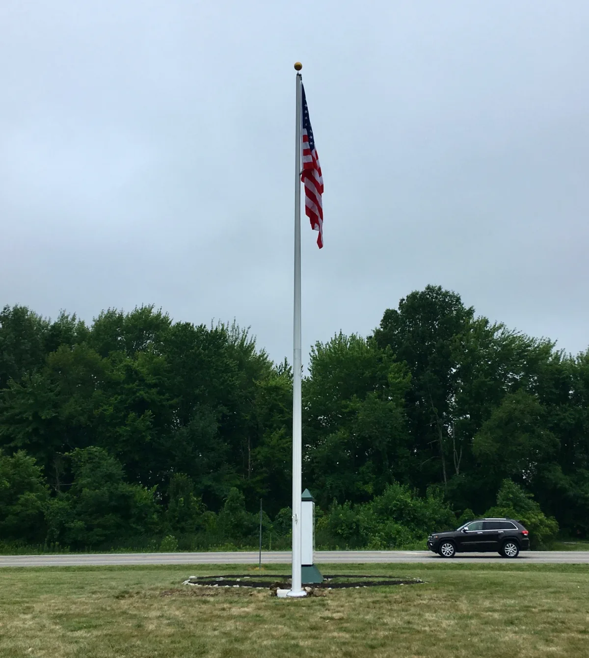 Roadside flagpole installation with memorial base and landscaped surround