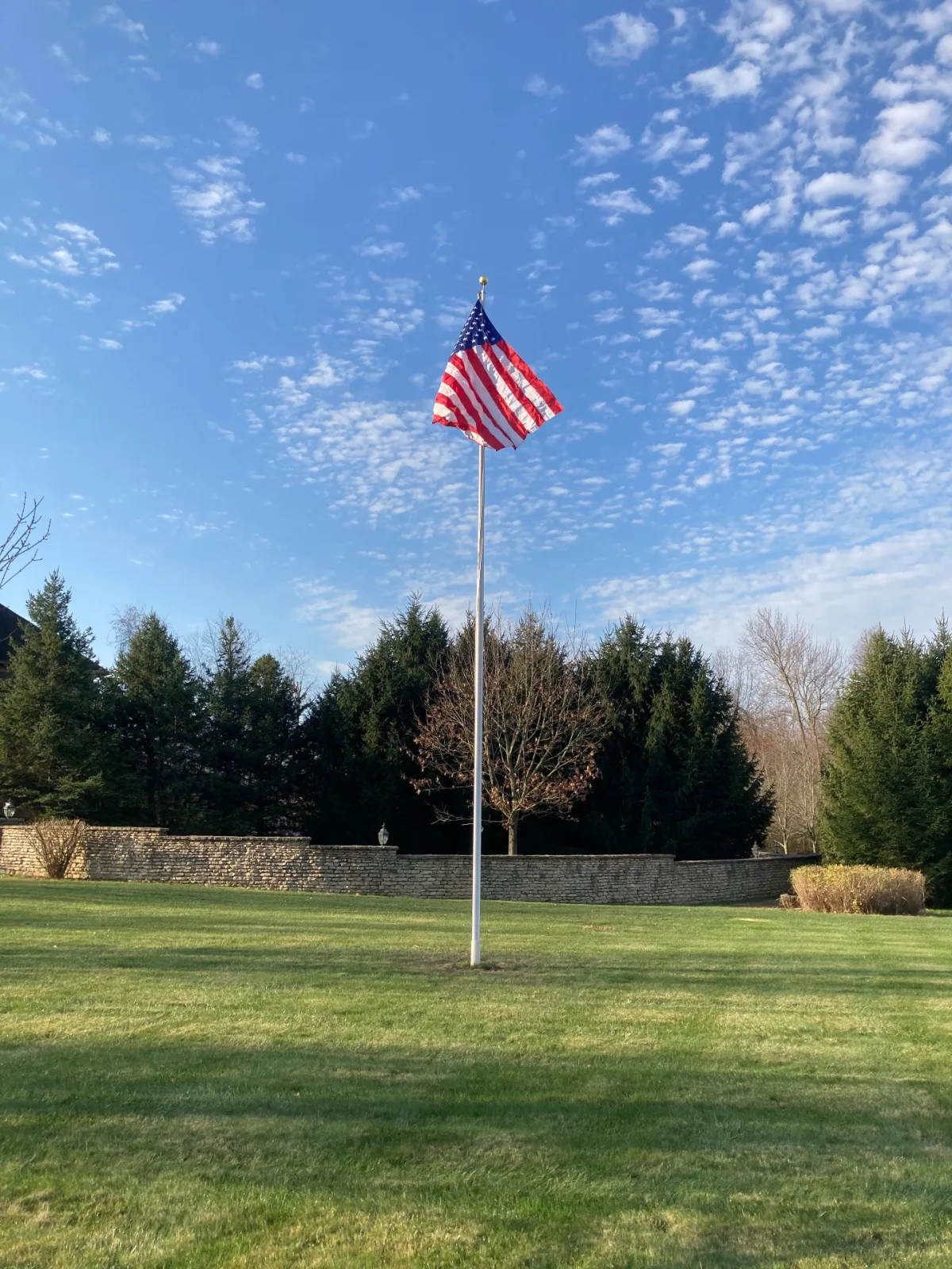 Residential flagpole on manicured estate lawn with stone wall backdrop