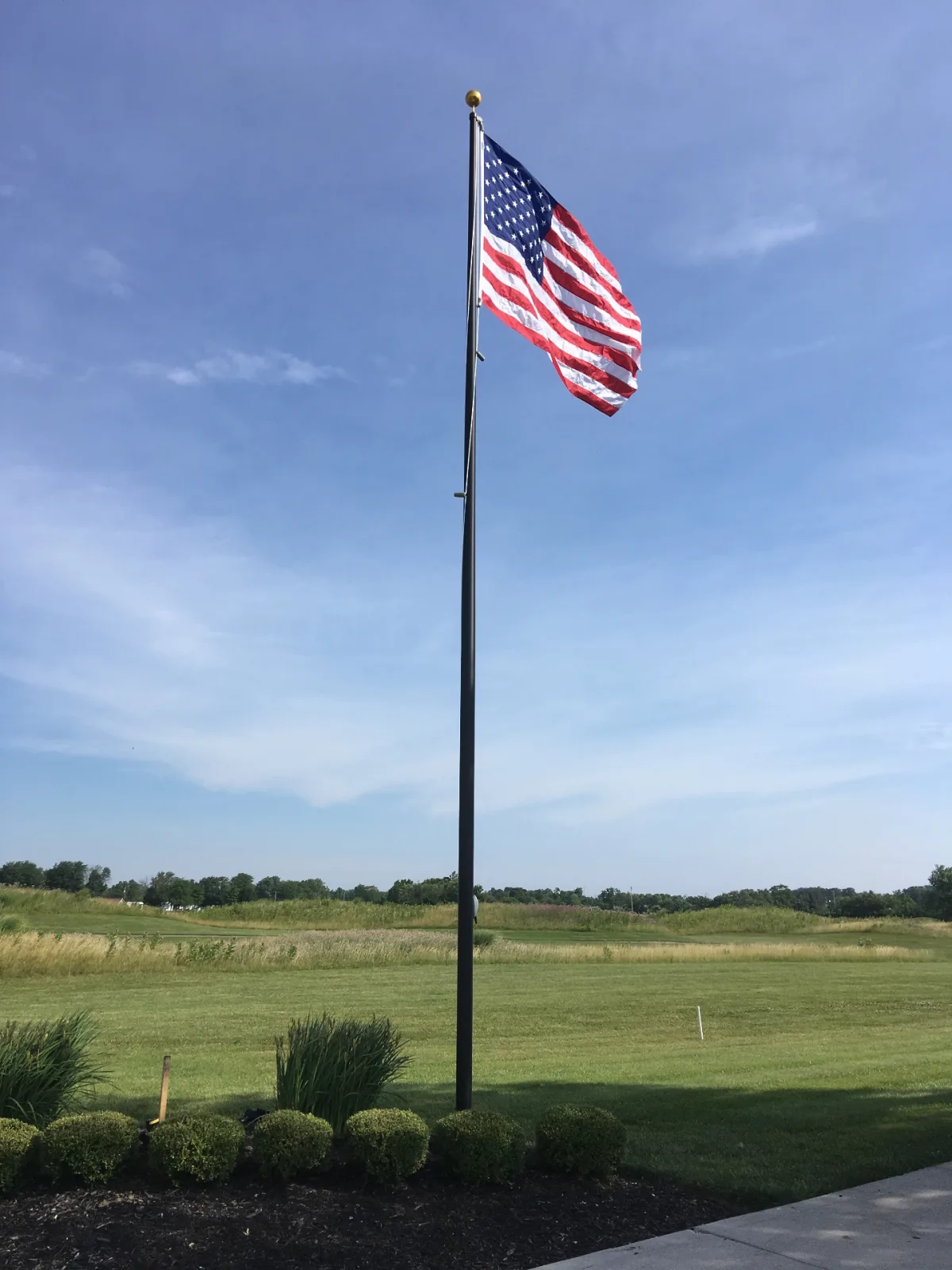 Black anodized residential flagpole flying American flag in open rural yard